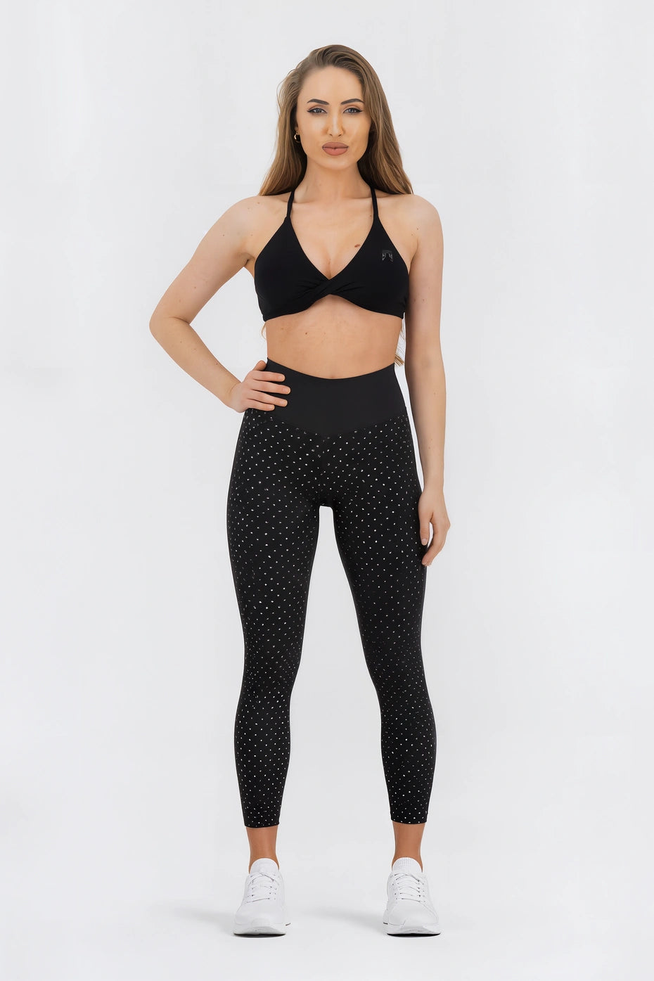 Woman wearing a black sports bra and leggings with white polka dots on a white background
